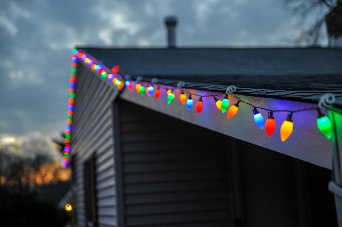 A home's roofline outlined in warm white Christmas lights at dusk